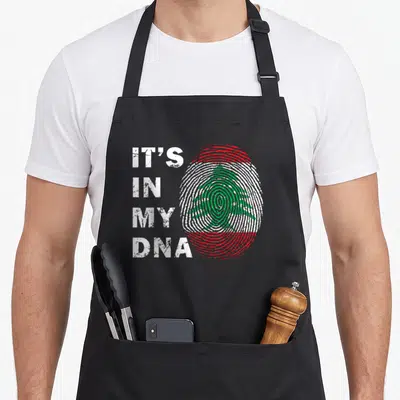 Lebanon lebanese girl apron - Fingerprint with green cedar tree and IT'S IN MY DNA text in red white green distressed — shown on a black cotton canvas apron against a white background