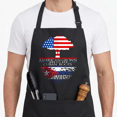Grown tree american flag apron - Tree with US flag canopy and Cuban flag roots and centered heritage text — shown on a black cotton canvas apron against a white background