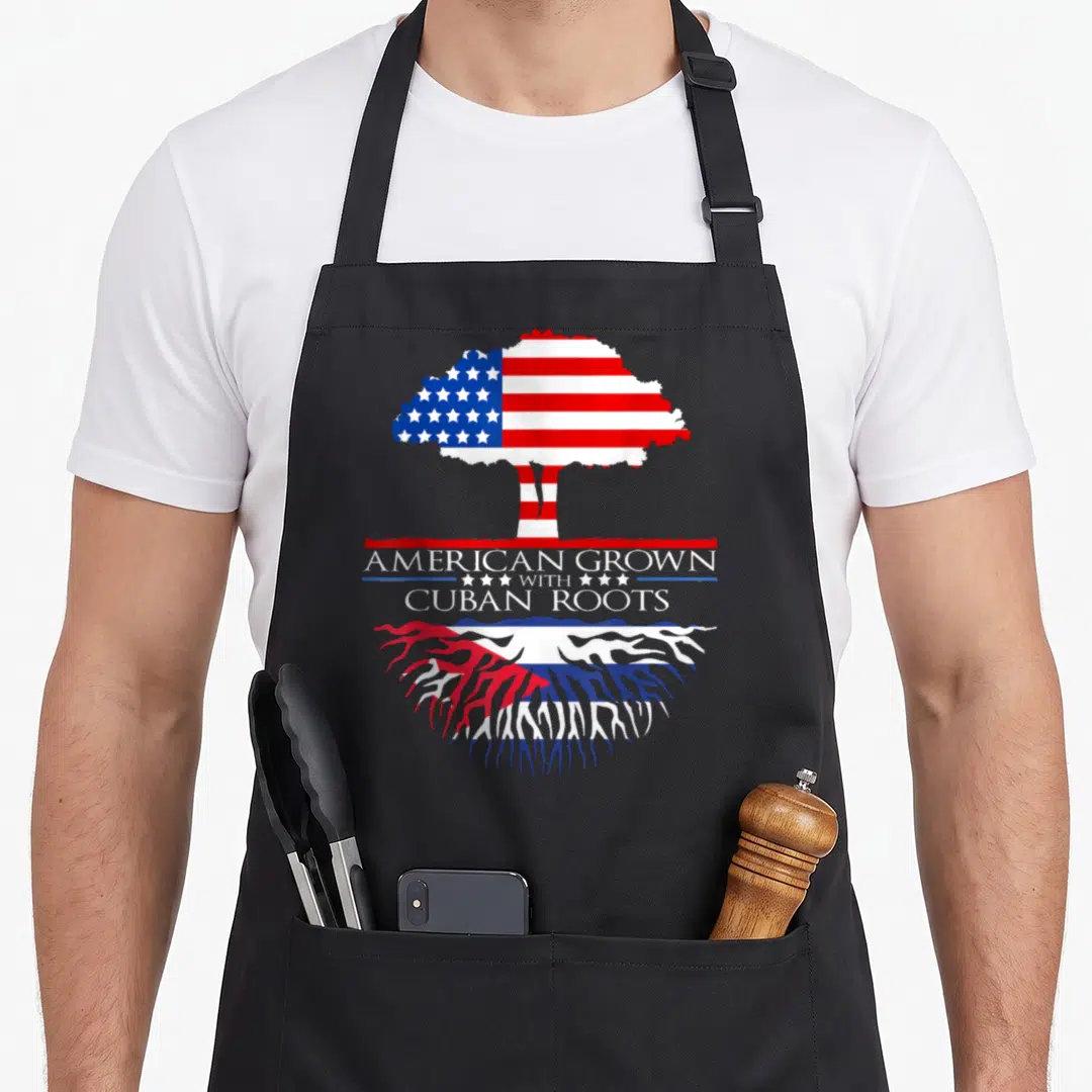 Grown tree american flag apron - Tree with US flag canopy and Cuban flag roots and centered heritage text — shown on a black cotton canvas apron against a white background