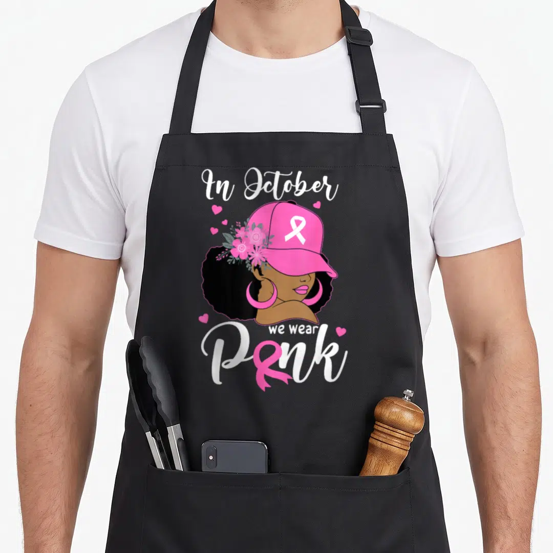 Cute october breast cancer awareness aprons - Cartoon woman in pink cap with ribbon and flowers surrounded by hearts — shown on a black cotton canvas apron against a white background