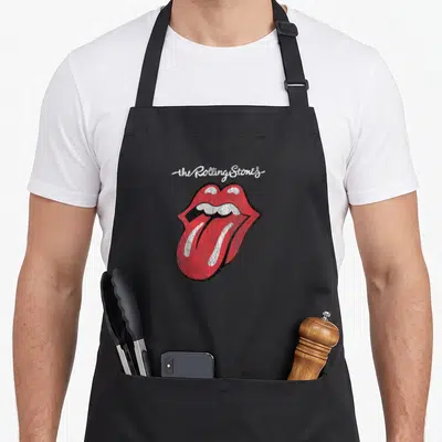 Fitness rolling stones apron - Distressed red lips with protruding tongue and white script text on black outline — shown on a black cotton canvas apron against a white background