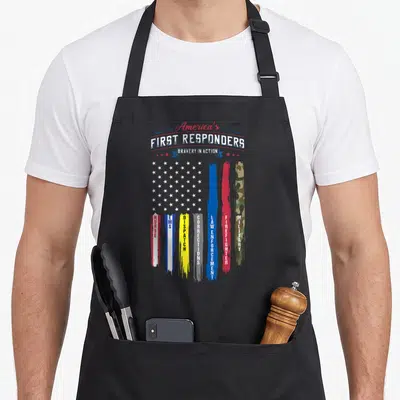 Americas american flag apron - Distressed USA flag with vertical stripes listing nurse, EMS, dispatch, corrections, law — shown on a black cotton canvas apron against a white background