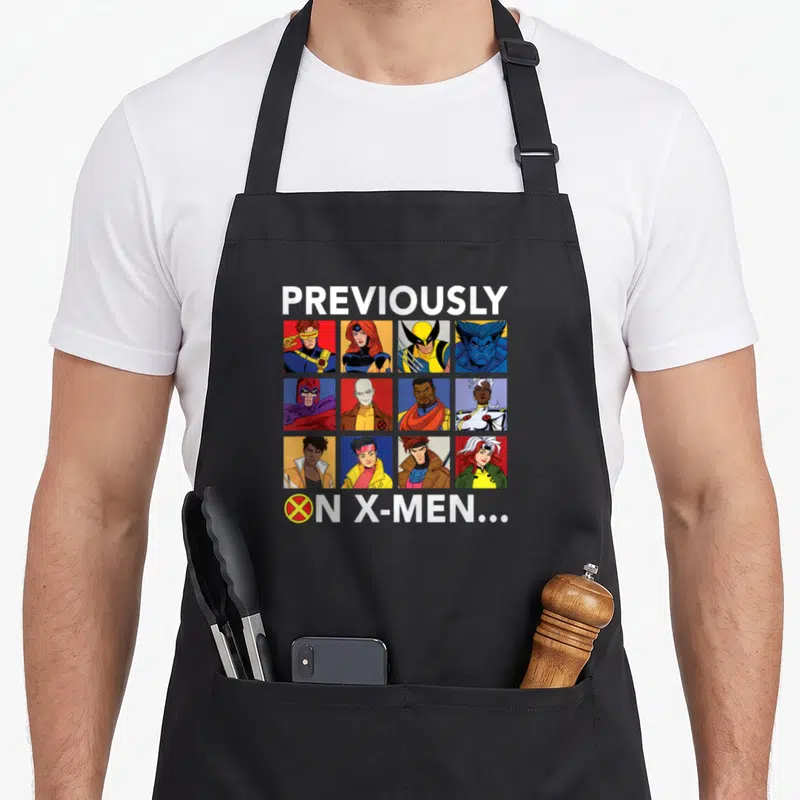 Previously x apron - Twelve character portraits in a grid below previously on X-men text — shown on a black cotton canvas apron against a white background