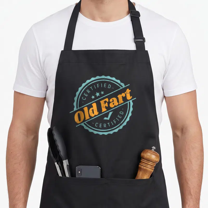 Fart birthday apron - Circular stamp reading CERTIFIED Old Fart in orange and distressed blue with stars and checkmark — shown on a black cotton canvas apron against a white background