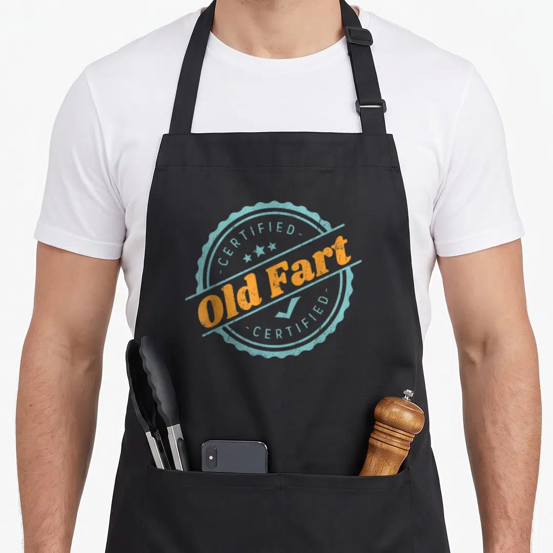 Fart birthday apron - Circular stamp reading CERTIFIED Old Fart in orange and distressed blue with stars and checkmark — shown on a black cotton canvas apron against a white background