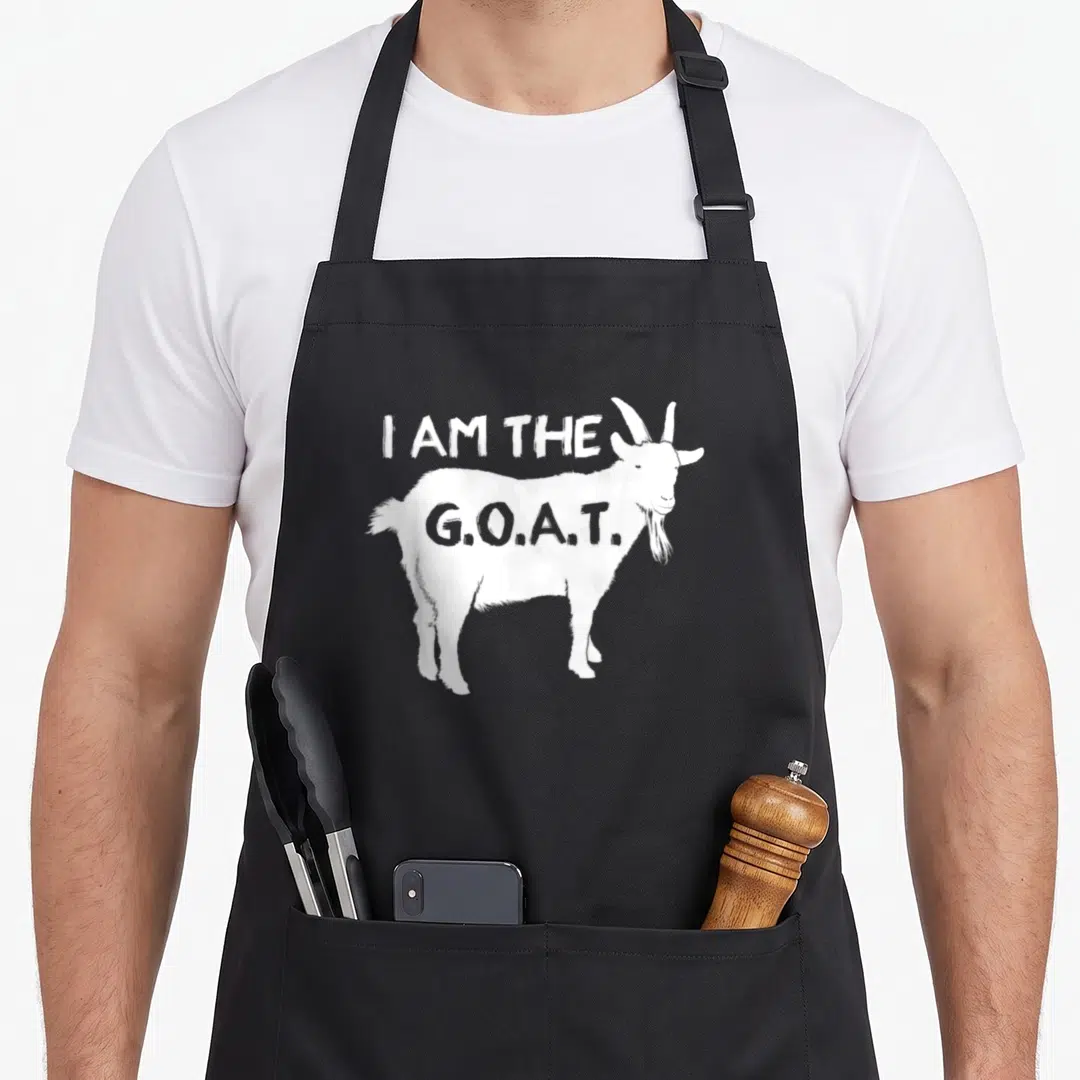 Athletic goat apron - White goat illustration with I AM THE G.O.A.T. text on black fabric — shown on a black cotton canvas apron against a white background