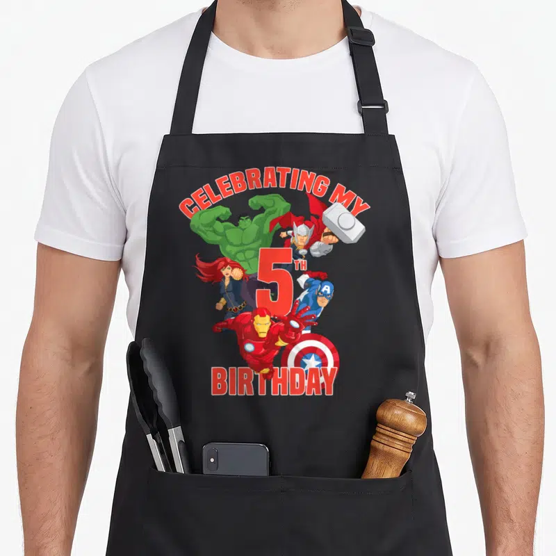 Celebrating birthday apron - Avengers cartoon characters surrounding red 5th birthday text on black apron — shown on a black cotton canvas apron against a white background