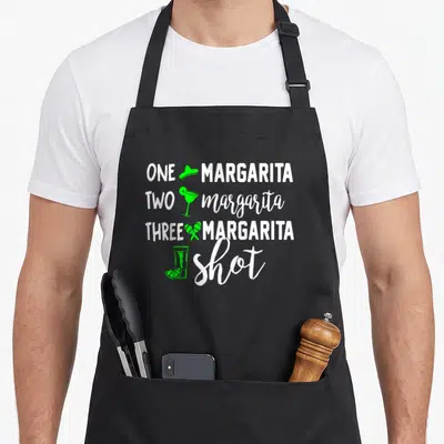 Three margarita apron - Stacked white text ONE MARGARITA TWO margarita THREE MARGARITA shot with green sombrero glass — shown on a black cotton canvas apron against a white background