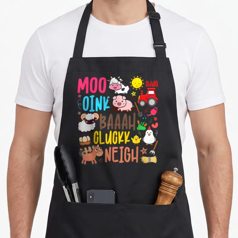 Cluck farm apron - Cartoon cow pig sheep horse chicken tractor with sound words MOO OINK BAAAH CLUCKK NEIGH in colorful — shown on a black cotton canvas apron against a white background
