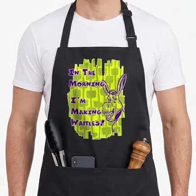 Waffle making aprons - Cartoon donkey head next to purple text IN THE MORNING I'M MAKING WAFFLES on lime green — shown on a black cotton canvas apron against a white background