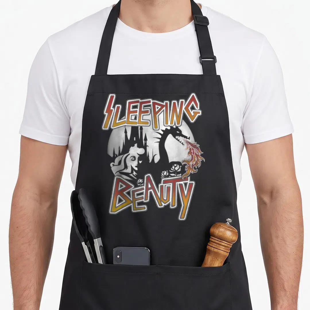 Rock beauty apron - SLEEPING BEAUTY text with dragon castle silhouette in retro orange yellow font — shown on a black cotton canvas apron against a white background