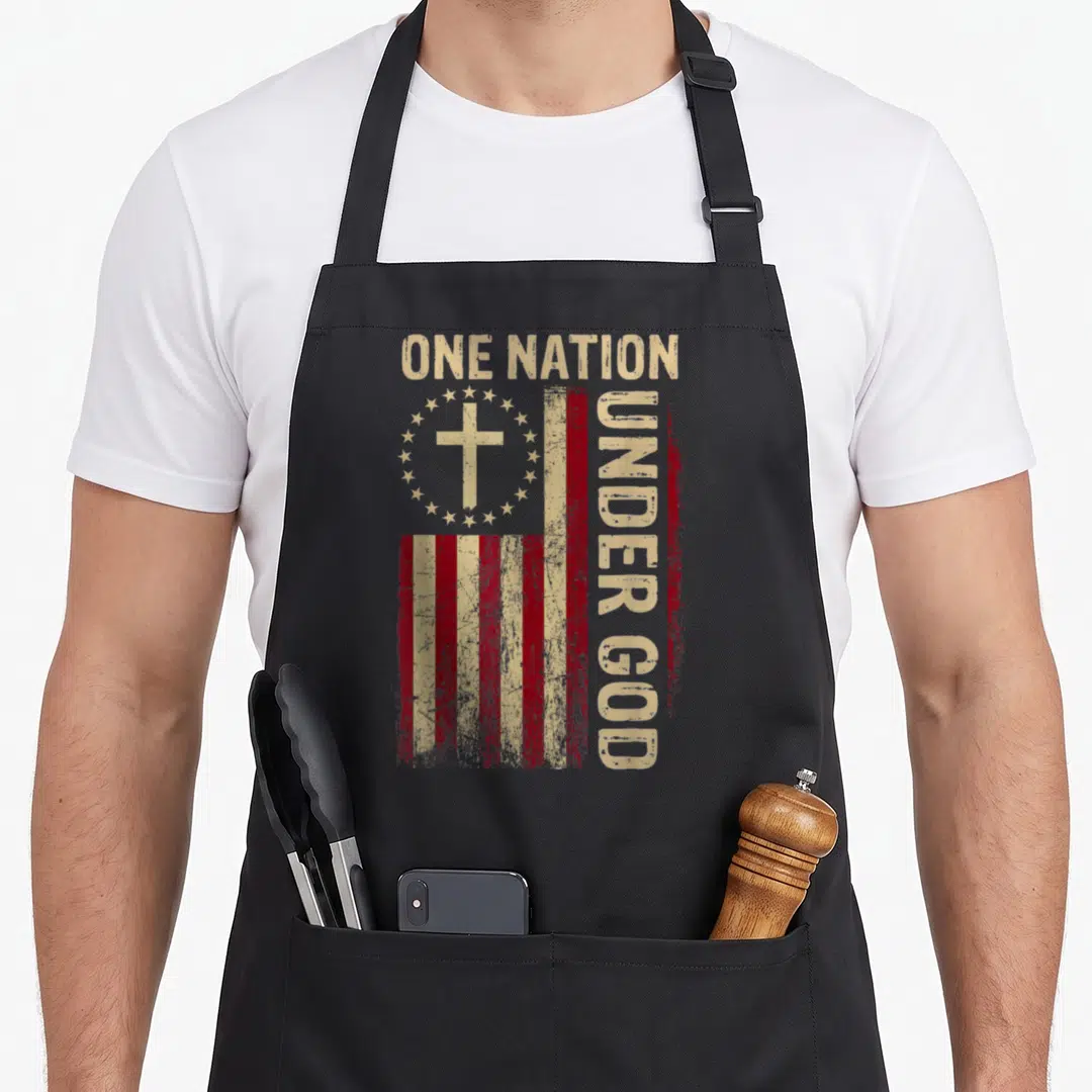 Nation 4th of july apron - Distressed red beige flag with cross stars and ONE NATION UNDER GOD text — shown on a black cotton canvas apron against a white background