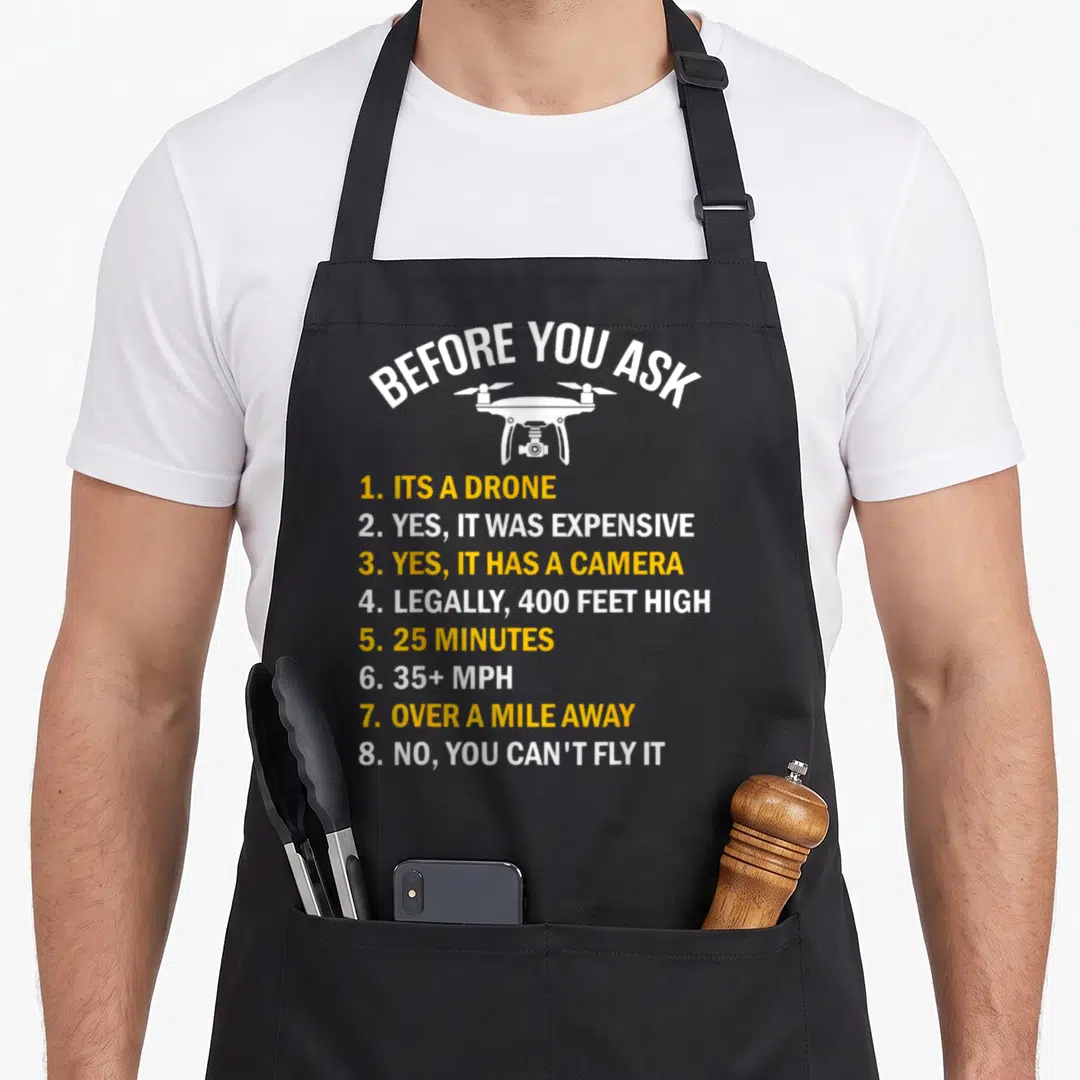Before drones apron - White drone illustration with arched text and yellow numbered list answering pilot questions — shown on a black cotton canvas apron against a white background