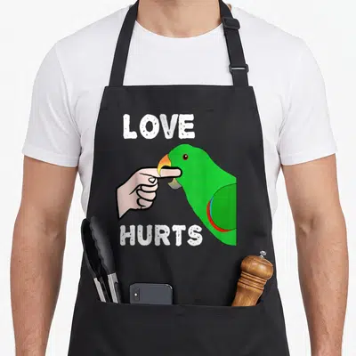 Eclectus love hurts apron - Green parrot biting pink finger with white LOVE HURTS text in cartoon style — shown on a black cotton canvas apron against a white background