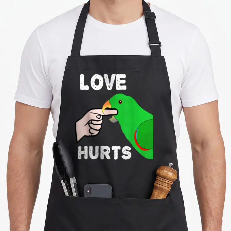 Eclectus love hurts apron - Green parrot biting pink finger with white LOVE HURTS text in cartoon style — shown on a black cotton canvas apron against a white background
