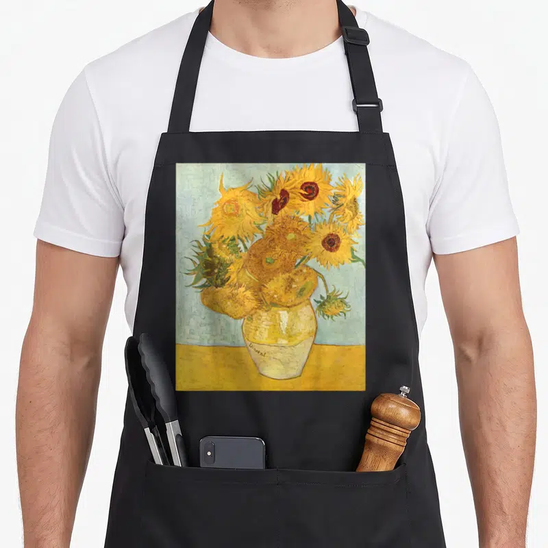 Vincent sunflower van gogh apron - Yellow sunflowers in a white vase marked Vincent on a blue background — shown on a black cotton canvas apron against a white background