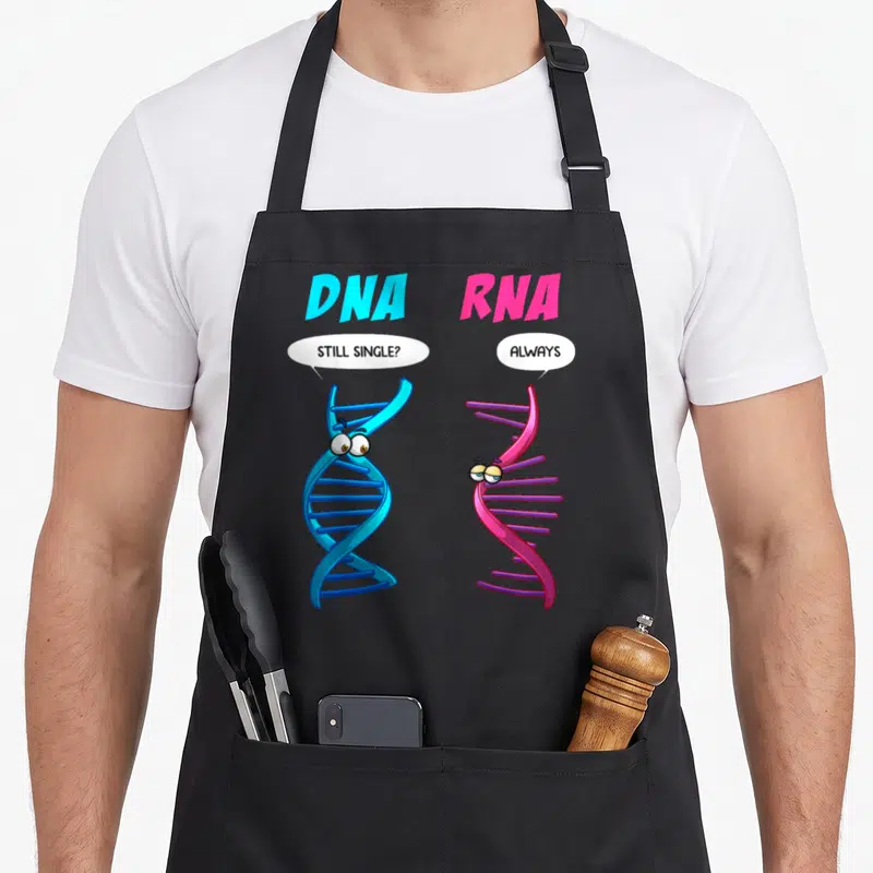 Dna biology apron - Blue DNA and pink RNA cartoon helices with speech bubbles reading still single always — shown on a black cotton canvas apron against a white background