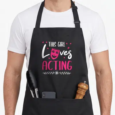 Actress acting apron - Stacked text THIS GIRL Loves ACTING with pink mask and white floral line — shown on a black cotton canvas apron against a white background