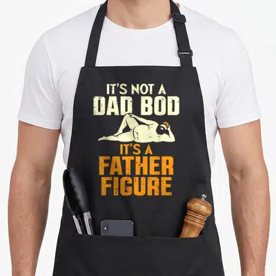 Bod grill daddy apron - Man lying down with It's Not A Dad Bod It's A Father Figure text — shown on a black cotton canvas apron against a white background