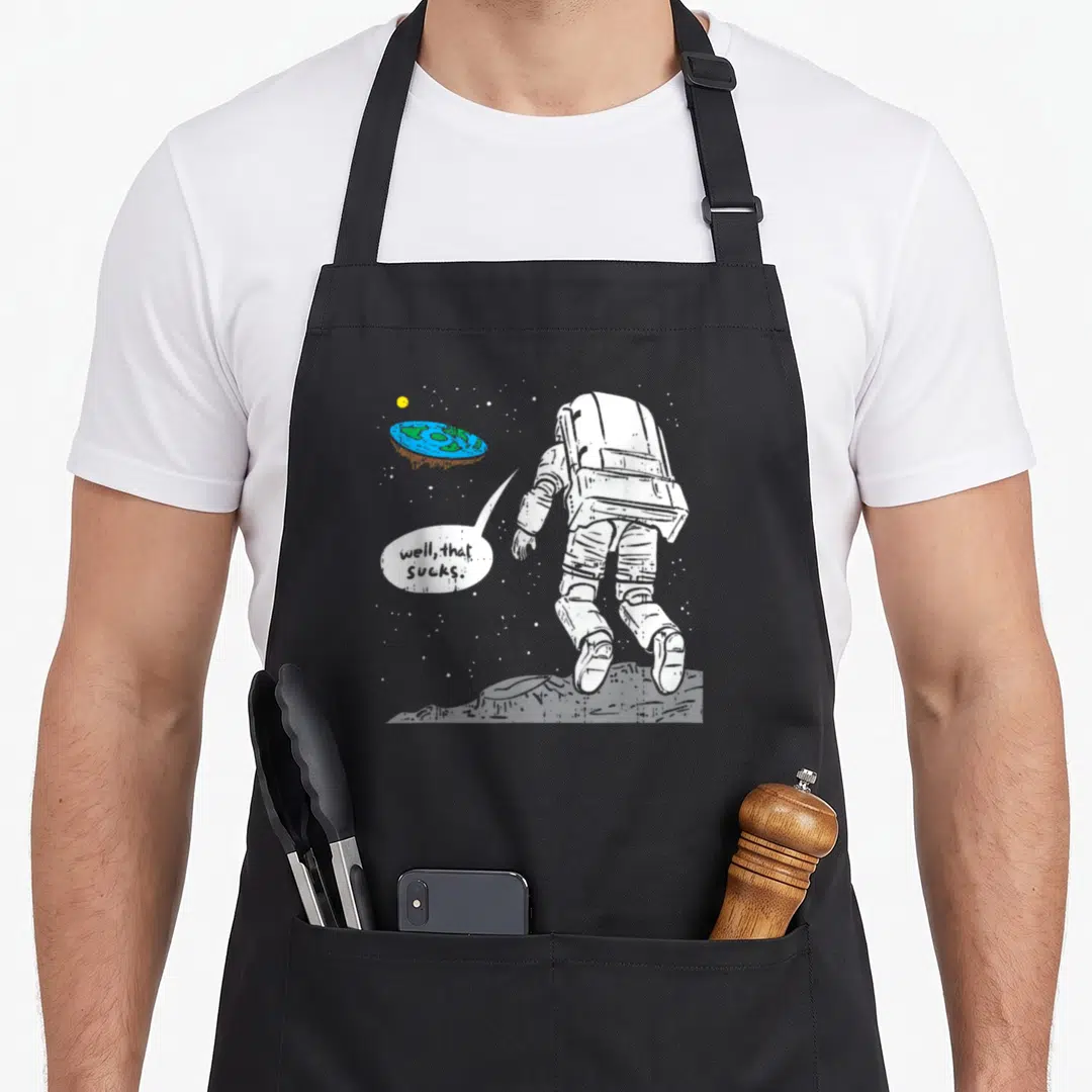 Moon earth apron - Astronaut on moon viewing flat blue green earth with speech bubble text well that sucks — shown on a black cotton canvas apron against a white background