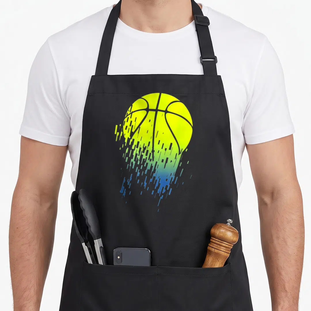 Disintegrating urban apron - Pixelated basketball graphic fading from yellow to green to blue in a digital glitch style — shown on a black cotton canvas apron against a white background