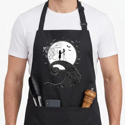 Funny sally jack apron - Skeleton couple silhouette on spiral hill under moon with bats and meant to be text — shown on a black cotton canvas apron against a white background