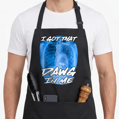 Dawg meme apron - Blue X-ray ribcage with pitbull head and white text I GOT THAT DAWG IN ME — shown on a black cotton canvas apron against a white background
