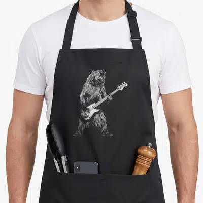 Guitar bear apron - Grey line art of a standing bear playing a four-string bass guitar — shown on a black cotton canvas apron against a white background
