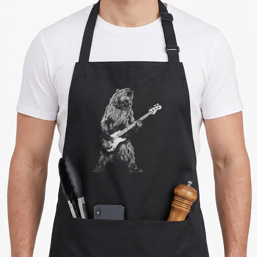 Guitar bear apron - Grey line art of a standing bear playing a four-string bass guitar — shown on a black cotton canvas apron against a white background