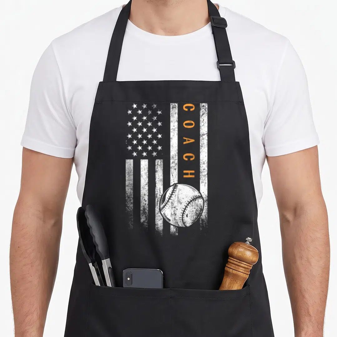 Trainer american flag apron - Distressed white flag with vertical orange COACH text and baseball graphic — shown on a black cotton canvas apron against a white background