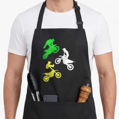 Toddler bike apron - Three motocross rider silhouettes in green, white, and yellow with distressed texture — shown on a black cotton canvas apron against a white background