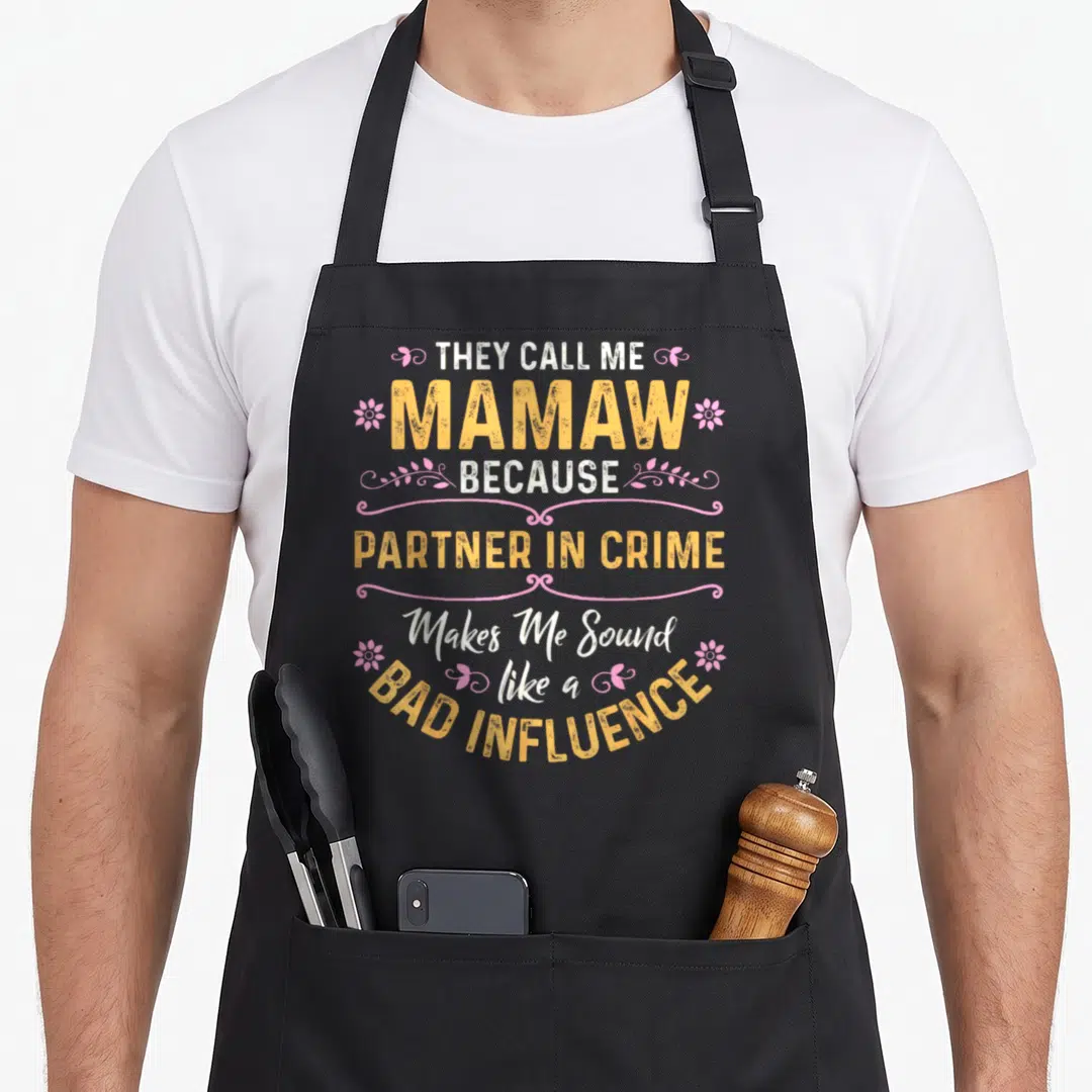 They crush first apron - Stacked yellow and white text reading They Call Me Mamaw Because Partner In Crime Makes Me — shown on a black cotton canvas apron against a white background