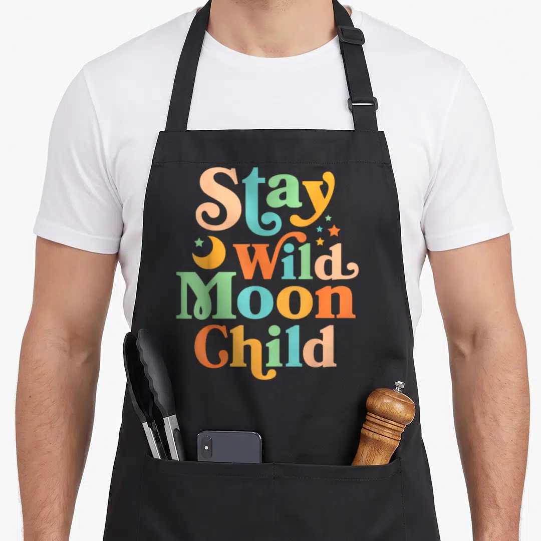 Stay 60s apron - Stay Wild Moon Child text in orange teal peach yellow green with moon and stars — shown on a black cotton canvas apron against a white background