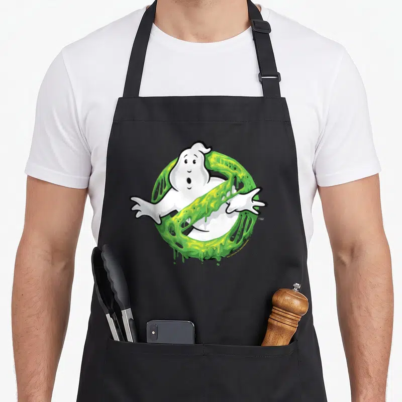 Slime ghost apron - Cartoon white ghost inside a ring of dripping green slime with black outlines — shown on a black cotton canvas apron against a white background