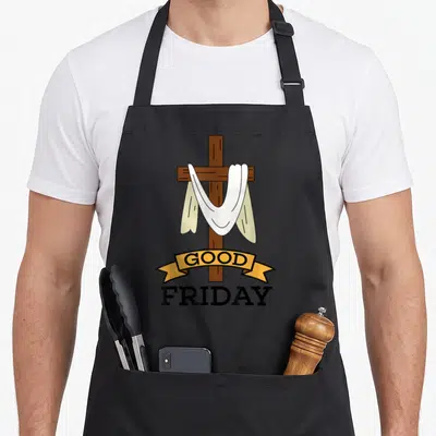 Fasting good friday apron - Brown cross with white shroud and yellow ribbon reading GOOD FRIDAY in black text — shown on a black cotton canvas apron against a white background