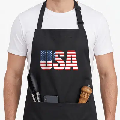 Cool patriotic 4th of july apron - USA text filled with red white and blue American flag pattern — shown on a black cotton canvas apron against a white background