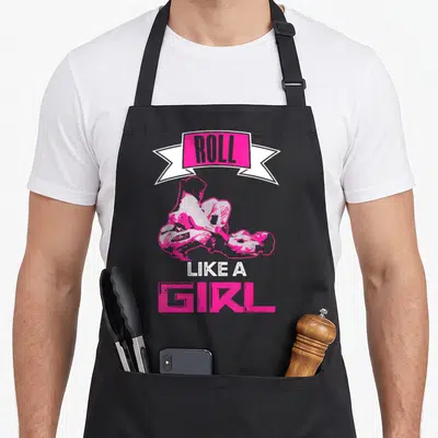 Roll brazilian jitsu apron - Pink cartoon of two grapplers with banner text ROLL LIKE A GIRL — shown on a black cotton canvas apron against a white background