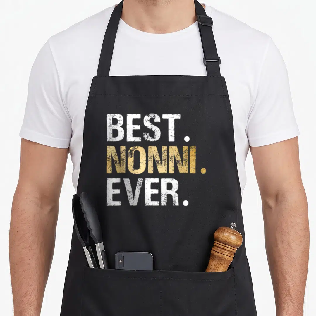 Grandparent christmas apron - Stacked white and gold distressed text reading best nonni ever on dark background — shown on a black cotton canvas apron against a white background