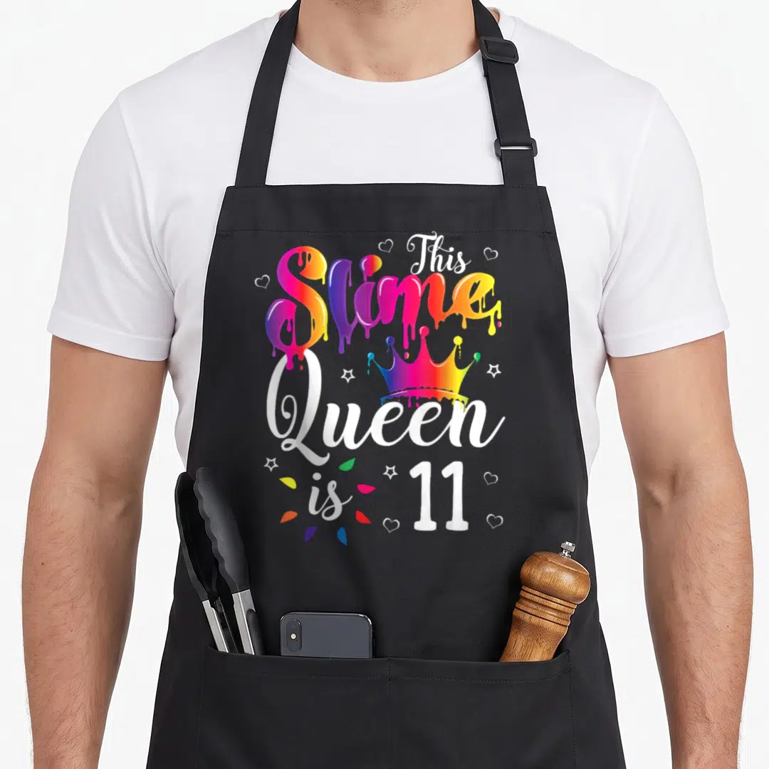 Slime queen of baking apron - Rainbow slime text and crown reading This Slime Queen is 11 — shown on a black cotton canvas apron against a white background