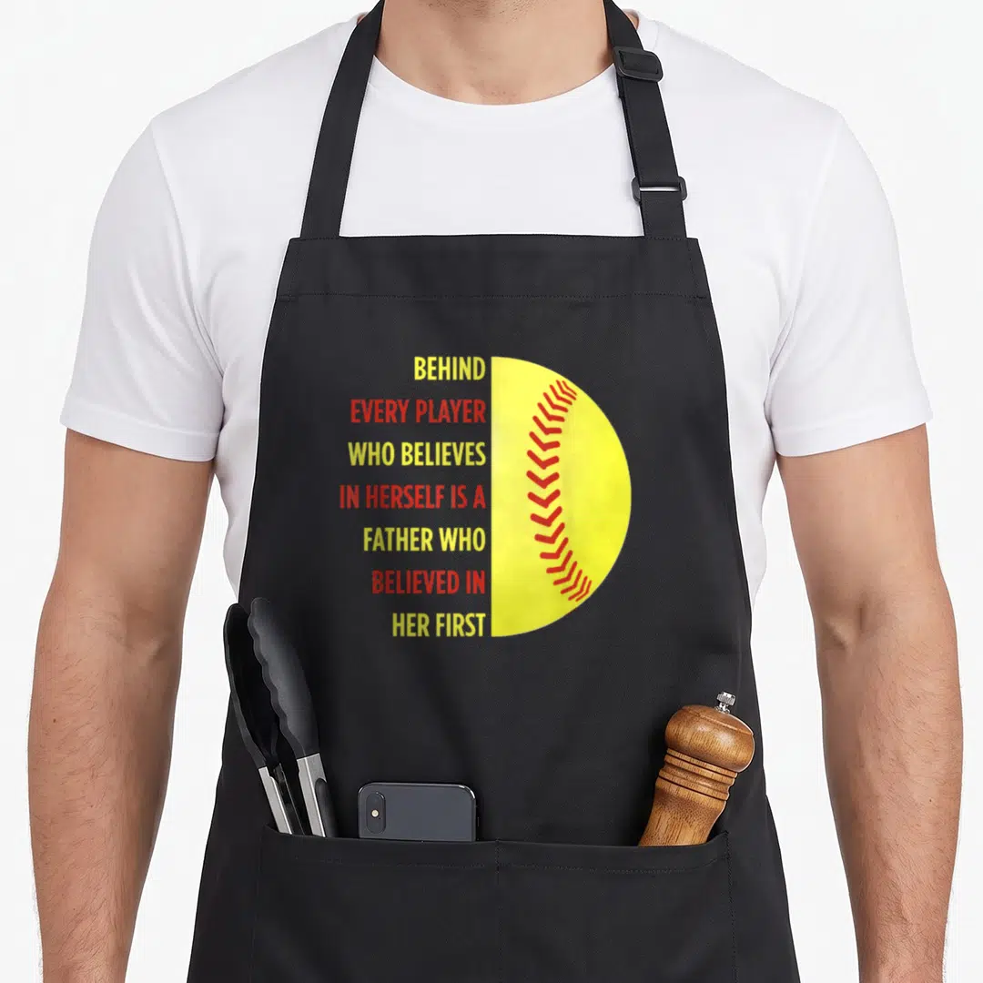 Behind father daughter aprons - Stacked yellow and red text next to a yellow half-softball with red stitching — shown on a black cotton canvas apron against a white background