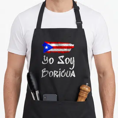 Soy puerto apron - Distressed Puerto Rico map filled with flag colors above stacked white text reading Yo Soy Boricua — shown on a black cotton canvas apron against a white background