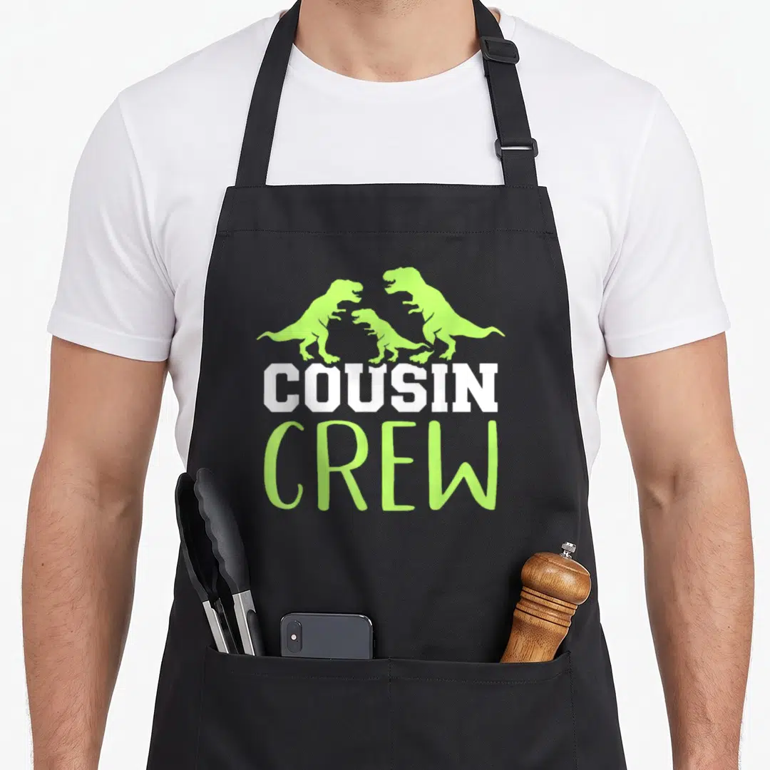 Vintage family crew apron - Three lime green dinosaur silhouettes above white COUSIN and green CREW text — shown on a black cotton canvas apron against a white background