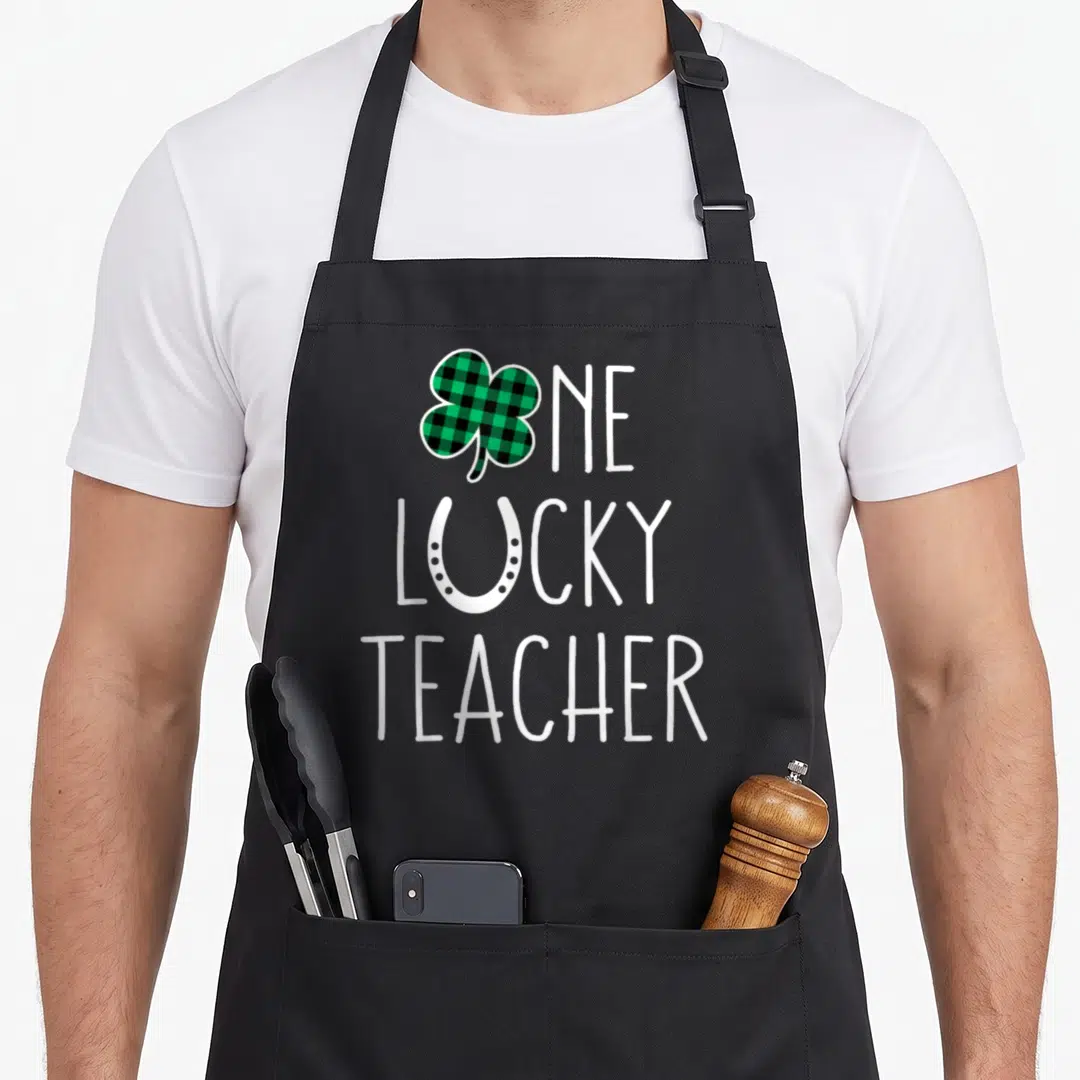 Prek st patrick day aprons - One Lucky Teacher text with plaid shamrock and white horseshoe typography — shown on a black cotton canvas apron against a white background