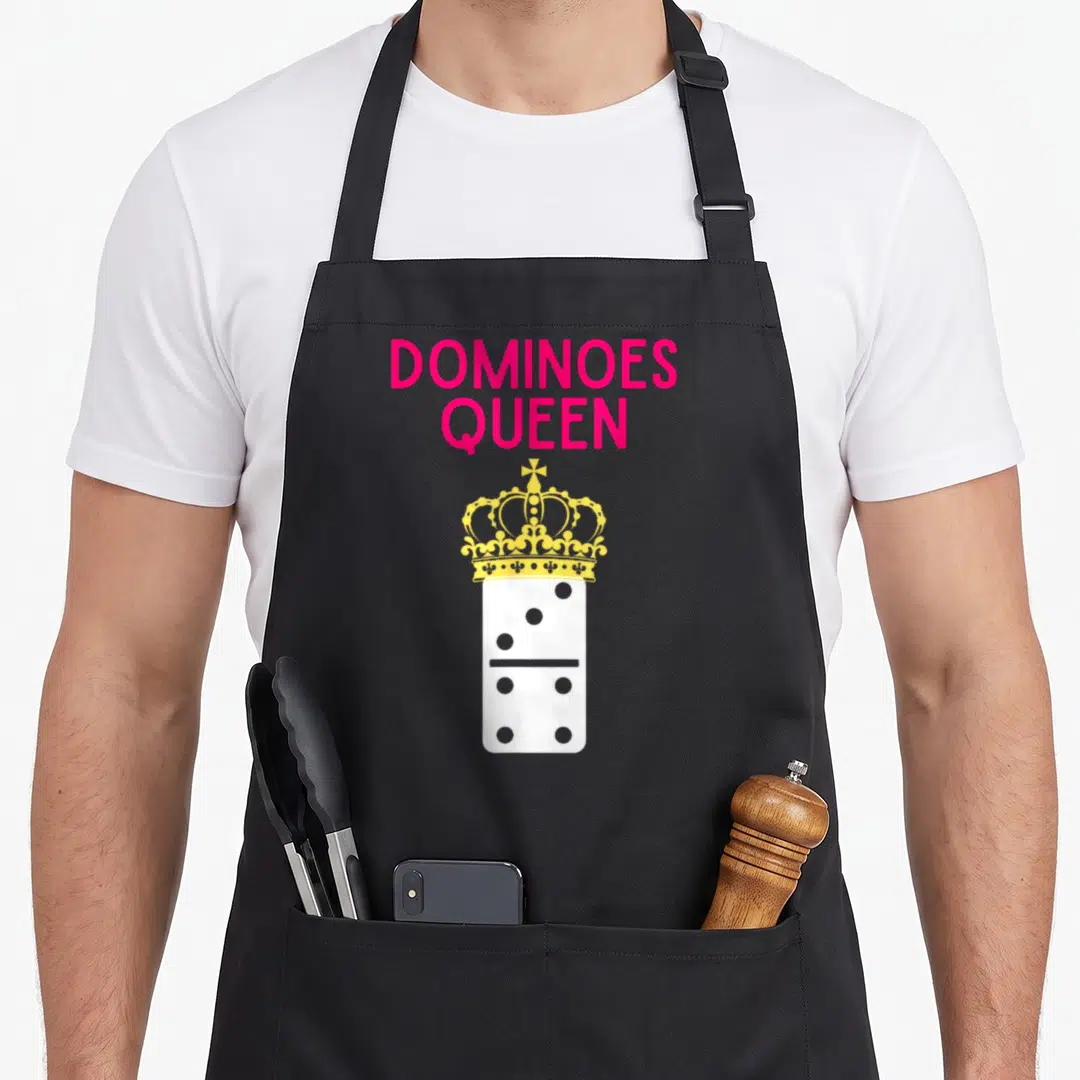Player queen apron - Pink DOMINOES QUEEN text above yellow crown on white domino tile — shown on a black cotton canvas apron against a white background