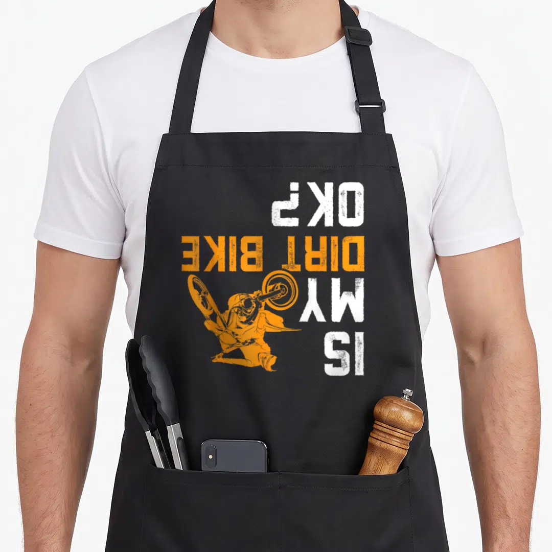 Motocross bike apron - Orange rider silhouette overlapping vertical white and orange text reading Is My Dirt Bike OK — shown on a black cotton canvas apron against a white background