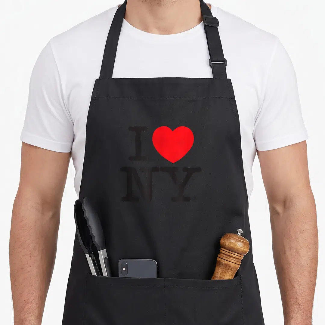 Funny new york apron - I NY text with red heart symbol on black background — shown on a black cotton canvas apron against a white background
