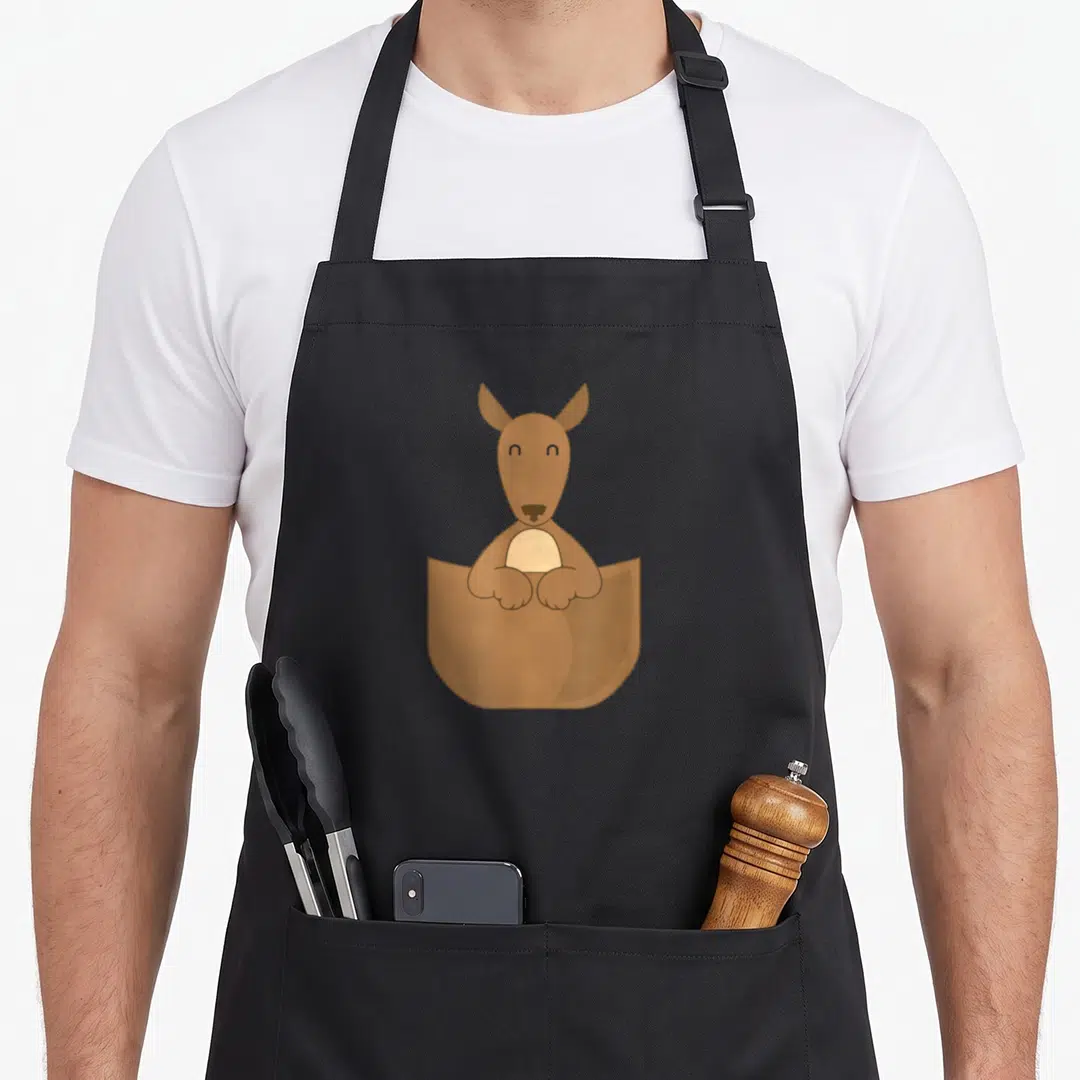 Pouch kangaroo apron - Cartoon brown kangaroo with tan belly peeking out of a pouch pocket — shown on a black cotton canvas apron against a white background