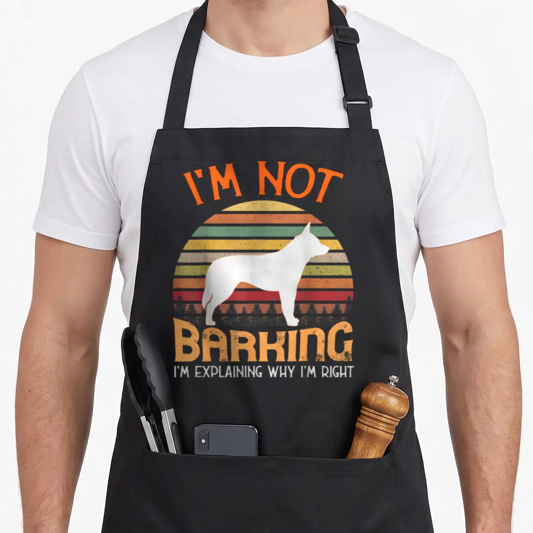 Blue heeler dog apron - White dog silhouette on striped retro sunset with text I'm Not Barking I'm Explaining Why I'm — shown on a black cotton canvas apron against a white background