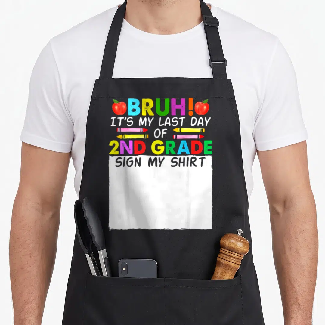 Signature 2nd apron - Colorful text BRUH IT'S MY LAST DAY OF 2ND GRADE flanked by two red apples and three pencils — shown on a black cotton canvas apron against a white background