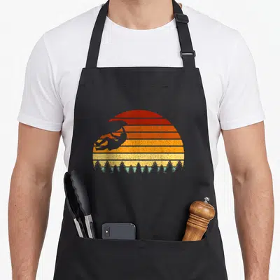 Boulderer bouldering apron - Retro striped sunset with grey climber silhouette and tree line — shown on a black cotton canvas apron against a white background